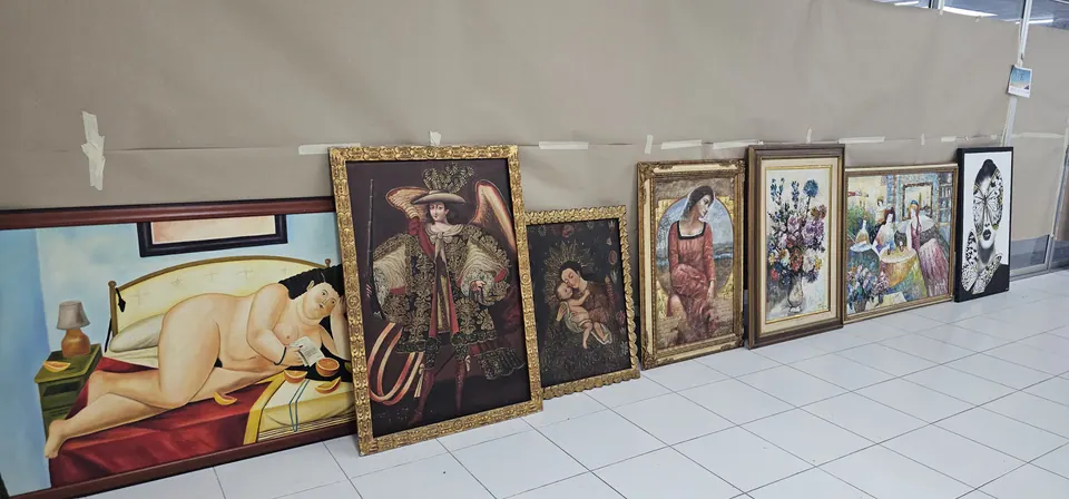 Framed paintings in gilded frames leaning in a row against a wall